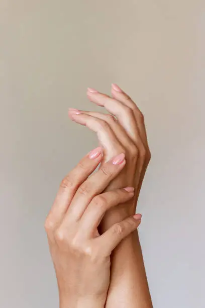Close up of a woman's hand with a perfect natural neutral delicate manicure on a beige background. A delicate color palette. Light nails in pastel colors