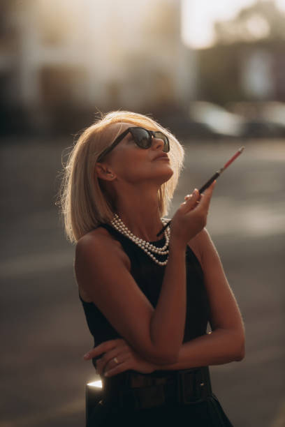 Mature woman smoking with mouthpiece. Blonde adult woman outdoors Mature woman smoking with mouthpiece. Blonde adult woman outdoors smoking women luxury cigar stock pictures, royalty-free photos & images
