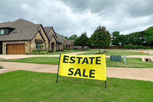 Outdoor shot of residential house with road and neat lawn in front of it, big yellow sign with estate sale inscription. Sale of mansions.