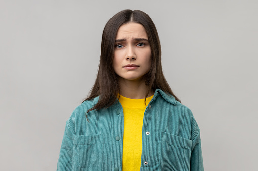 Portrait of disappointed woman being upset of bad news, looking at camera with frowning face, expressing sadness, wearing casual style jacket. Indoor studio shot isolated on gray background.