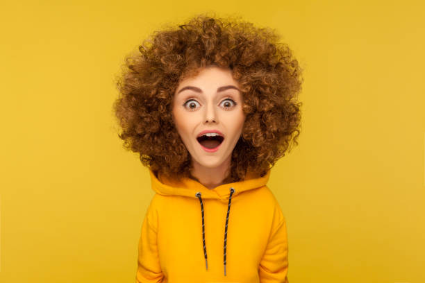 Surprised shocked funny woman looking at camera with open mouth and amazed big eyes. Wow, unbelievable. Comic portrait of shocked surprised funny woman with Afro hairstyle looking at camera with open mouth and amazed big eyes. Indoor studio shot isolated on yellow background. caricature stock pictures, royalty-free photos & images