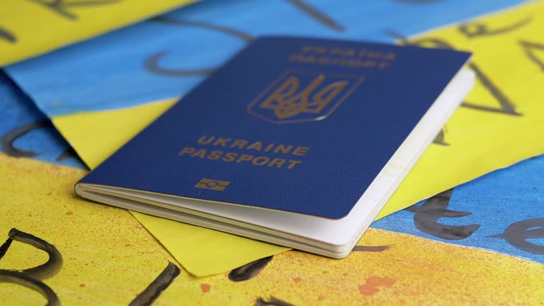 Hand Puts a Biometric Passport of Ukraine on a Background of Ukrainian Flag