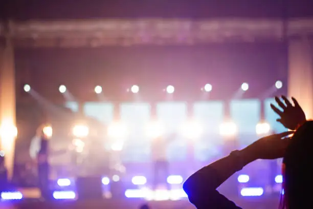 Photo of Defocus silhouette of one woman raise hand up in music concert with purple and white color spotlight on stage background. Copy space. Out of focus