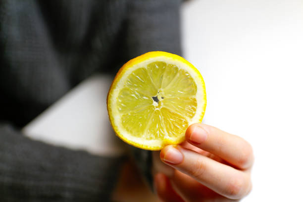 istock Defocus female hand holding one yellow slice lemon fruit. Hand holds lemon slice on white background. Closeup. Out of focus 1439322862