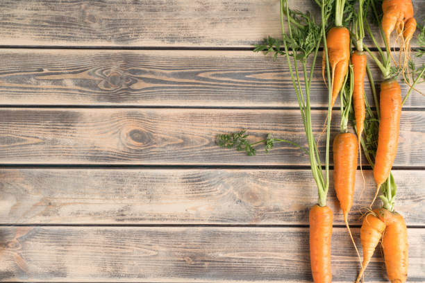 Vertical line of fresh ripe carrots on faded wooden table, top view. Raw vegetables arranged in order. Organic food or healthy diet concept. Location of objects. Planking. Place for text. línea vertical de zanahorias maduras frescas sobre mesa de madera descolorida, vista superior. verduras crudas dispuestas en orden. concepto de alimentación ecológica o dieta saludable. ubicación de objetos. tablazón. lugar para el texto