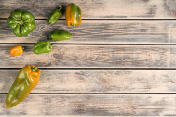 Bunch of small and big bell peppers on faded wooden table, top view. Green and yellow fresh vegetables. Food or healthy diet concept. Separated location of objects. Planking. Place for text. un montón de pimientos pequeños y grandes en una mesa de madera descolorida, vista superior. verduras frescas verdes y amarillas. concepto de alimentación o dieta saludable. ubicación separada de los objetos. tablazón. lugar para el texto