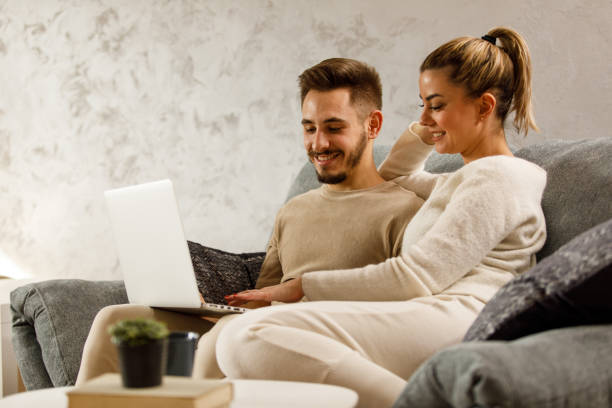 istock Couple relaxing on the sofa, smiling at each other, looking at home decor online 1439326607