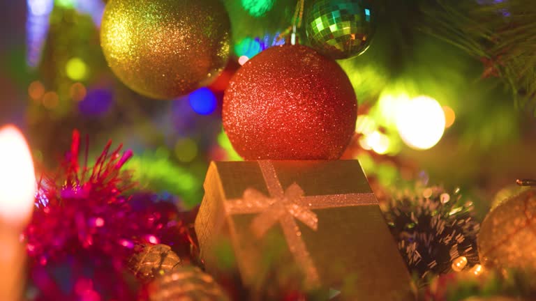 Christmas decorations of different colors with glitter hang next to the gift box.