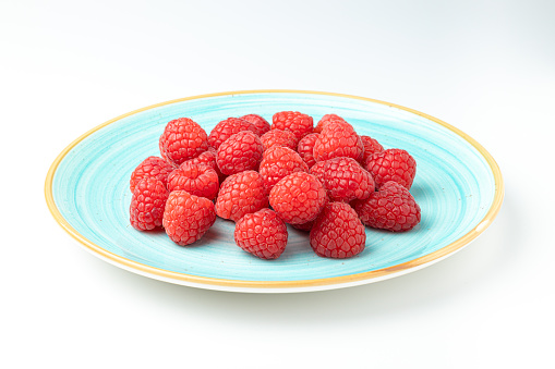 sky blue plate full of raspberries on white background