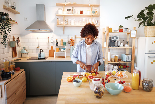 Young beautiful woman cutting fruits for a smoothie in her kitchen