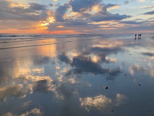 istock Distant people walk on a dramatic pink and blue cloudscape reflected on the sand at the beach 1439332723