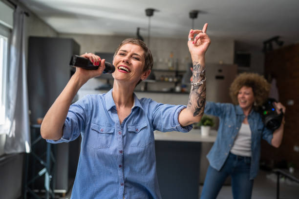 Two women adult mature caucasian friends or sisters having fun at home females dancing and singing karaoke hold microphone listen to the music happy smile joyful rhythm real people copy space stock photo