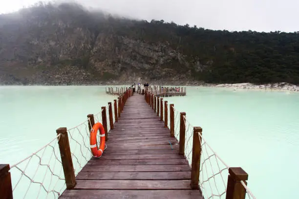 Wooden jetty inside Kawah Putih or White Crater which is a volcanic lake inside a volcanic crater. Sulphur or Sulfur is emitted from within the volcano and yellow deposits can be found all around the edges of the lake. Also fumaroles can be seen around the edges of the caldera. The location is a popular hotspot for visitors and is located near the towns of Ciwidey and Soreang and the city of Bandung in West Java Province in Indonesia.