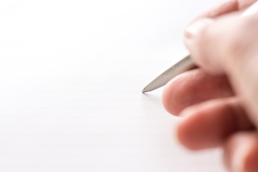 Woman's hand holding ballpoint pen against blank lined paper ready to start writing