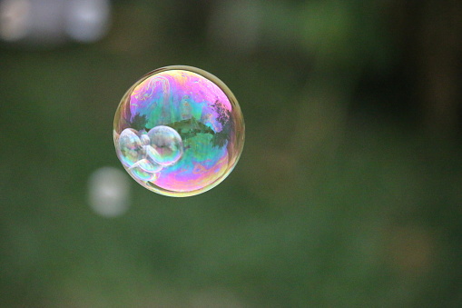 Shiny iridescent and translucent soap bubble floating in the air above green grass.