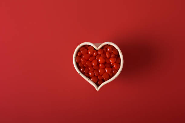 Heart candies in handmade ceramic bowl on red background.  Flat lay.