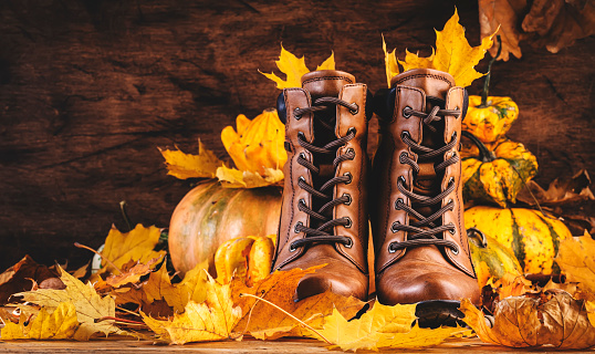Autumn background with brown leather boots, pumpkins, maple and oak leaves on rustic wood background,. Country style female stylish shoes. Copy space banner