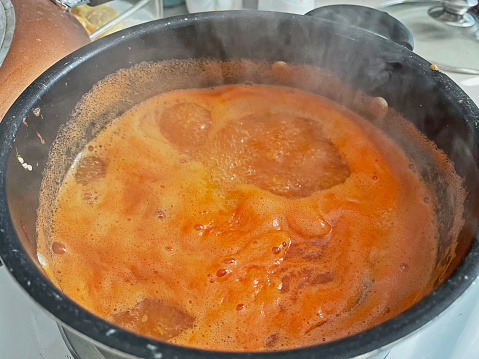 A pot filled of tomato sauce.   Boiling with steam rising.