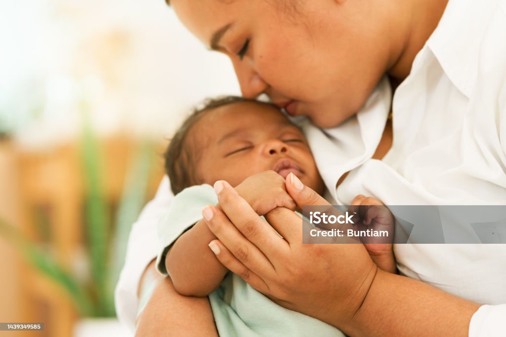 Newborn baby one-month-old holding fingers mother's hand. African Newborn baby one-month-old holding fingers mother's hand, sleep relax worry-free in warm embrace mom. image with a shallow depth of field, Select focus area hand. concept family mixed race. Baby - Human Age Stock Photo