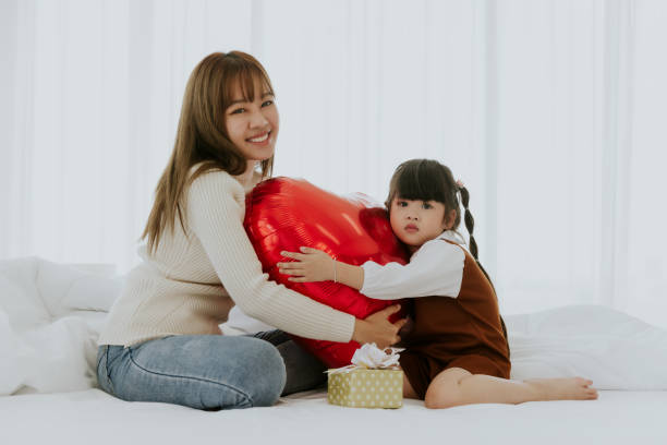 寝室で小さな4歳の子供の娘と遊ぶ心の風船を持って微笑むアジアの若いお母さん、母の日のコンセプト - 20 25 years adult bed bedroom スト��ックフォトと画像
