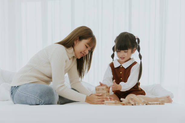 Mom and little 4 years old kid daughter with computer laptop playing education wooden box puzzle toy together at living room stock photo