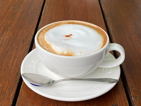 Cappuccino coffee in white coffee cup on wooden table