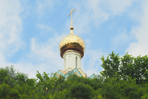 Golden dome and cross of the Christian church against the blue sky and clouds.