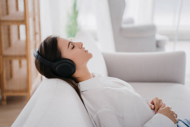 Young student caucasian girl in white shirt and headphones on her head, relaxing on sofa at home eyes closed, listening music, preparing to exams. Young calm woman at home sleeps sitting on sofa. joven estudiante caucásica con camisa blanca y auriculares en la cabeza, relajándose en el sofá de casa con los ojos cerrados, escuchando música, preparándose para los exámenes. una mujer joven y tranquila en casa duerme sentada en el sofá.