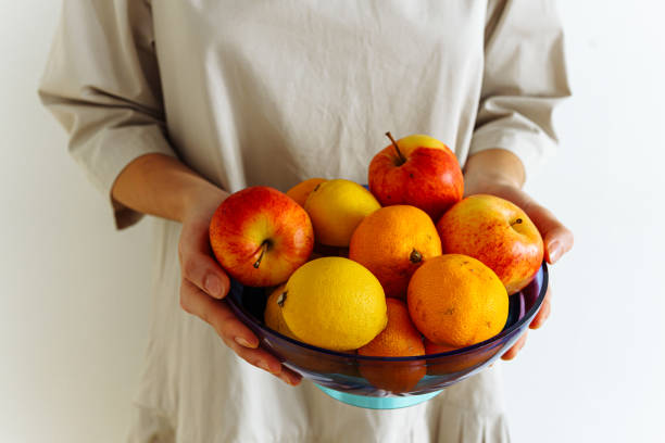 Citrus tangerines oranges and apples in fruit plate, in hands of young unrecognizable woman in beige dress