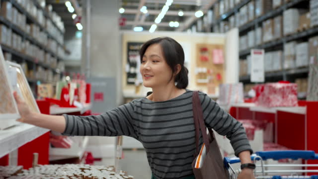 Asian woman with shopping cart walking and choosing Christmas decoration in store.