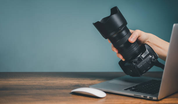 istock Buy Camera Online concept, Hand holding camera and sticking out form the Laptop computer monitor screen. 1439388687