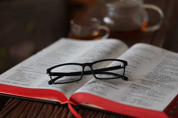 The New King James Version of the Holy Bible is placed on a richly grained Rosewood table. It is open at the Book of Psalms. The reader's eyeglasses have been placed on the open Bible, indicating he has taken a break. A ribbon bookmark is visible.  Indoor studio close-up shot; copy space. No people.