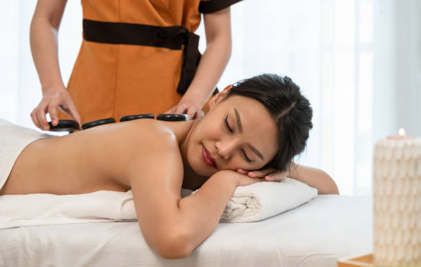 スパサロンでリラックスして楽しんでいる美しい若い女性と、体に熱い石のマッサージ。エステセラピー - lastone therapy spa treatment massaging massage therapist ストックフォトと画像