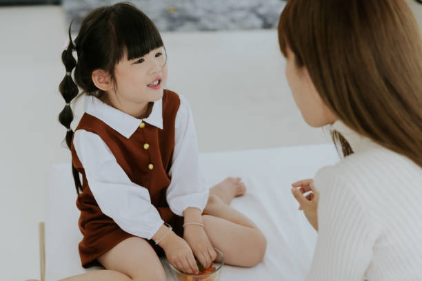 アジアの若い母親と4歳の子供の娘が笑顔で横たわり、白いベッドで一緒にキャンディーを食べて遊ぶ、幸せな素敵な家族のコンセプト - 20 25 years adult bed bedroom ストックフォトと画像