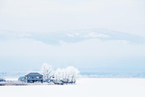 Snow-covered house and trees on the mountain lake during snowfall. Beautiful winter landscape. South Ural, Russia