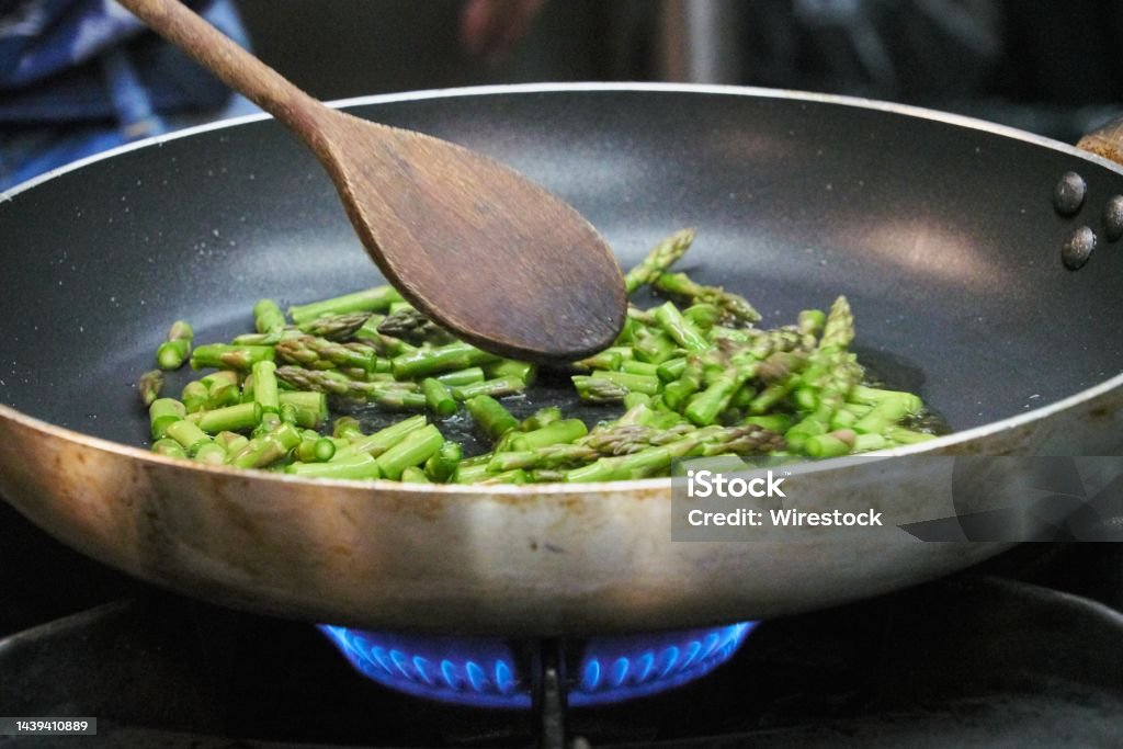 Closeup of asparagus sauteed in a non-stick pan with a wooden ladle A closeup of asparagus sauteed in a non-stick pan with a wooden ladle Cooking Pan Stock Photo