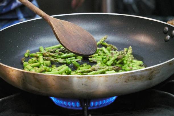 Closeup of asparagus sauteed in a non-stick pan with a wooden ladle A closeup of asparagus sauteed in a non-stick pan with a wooden ladle sauteed stock pictures, royalty-free photos & images