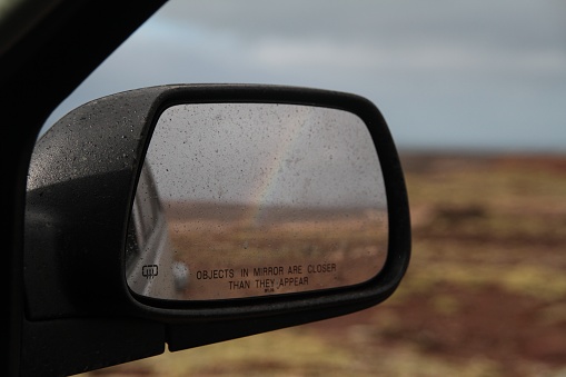 A closeup shot of the car mirror reflecting the rainbow