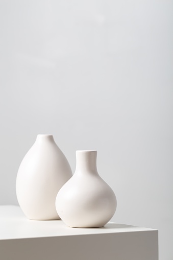 A closeup of two white clay vases on the table under the lights against a white background