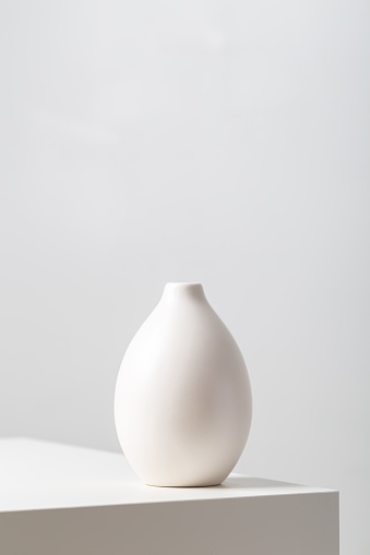 A vertical closeup of a white clay vase on the table under the lights against a white background
