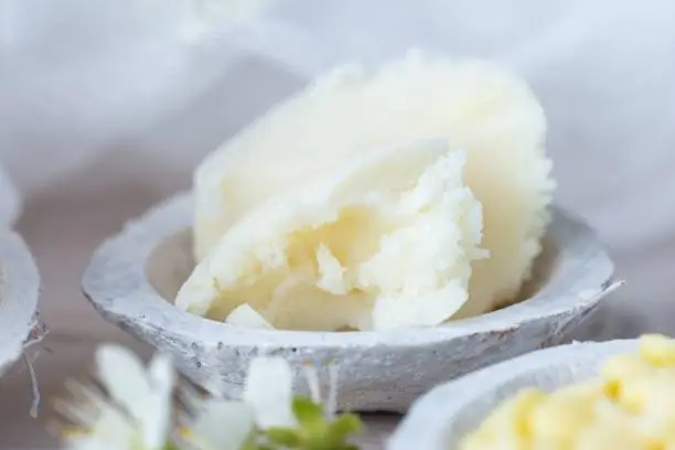 A selective focus shot of shea butter in a saucer and some white flowers on a white table top