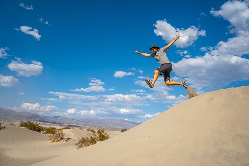 A male jumping in a desert in the Death Valley, California, the United States with the blue sky in the background