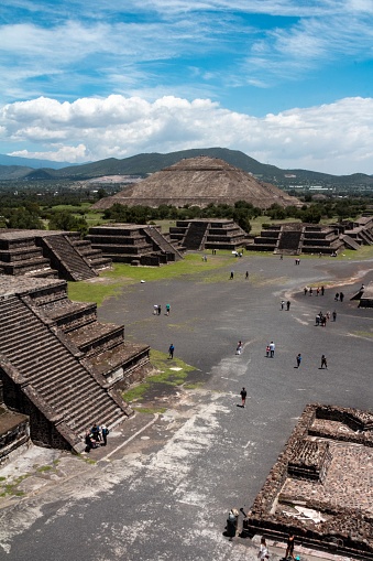 A vertical shot of people touring in Teotihuacan Pyramids in Mexico with a cloudy blue sky in the background
