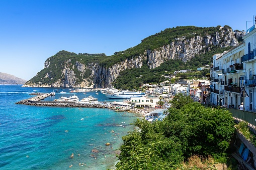 A beautiful view of Marina Grande harbor in Capri, Campania, Italy on a sunny day with Punta del Capo in the background