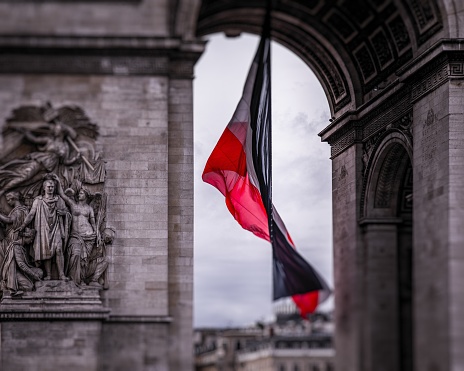 A closeup shot of a French flag  in front of the Triumphal Arch of the Star, Paris, France