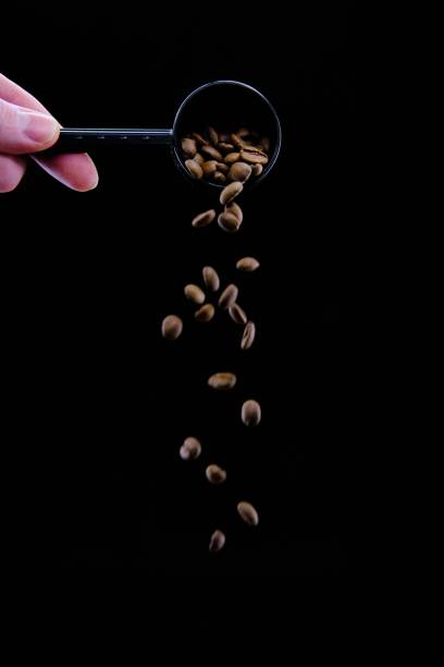 Vertical shot of coffee beans dropping from a coffee scoop isolated on a black background