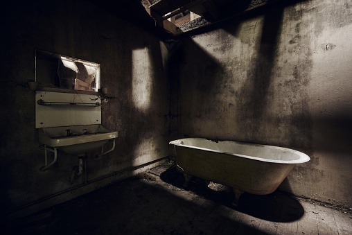An abandoned bathroom with a sink on the wall under a ruined ceiling at daytime