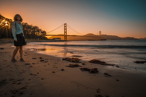 A girl standing next to the Golden Gate Bridge in San Francisco, USA during a sunset