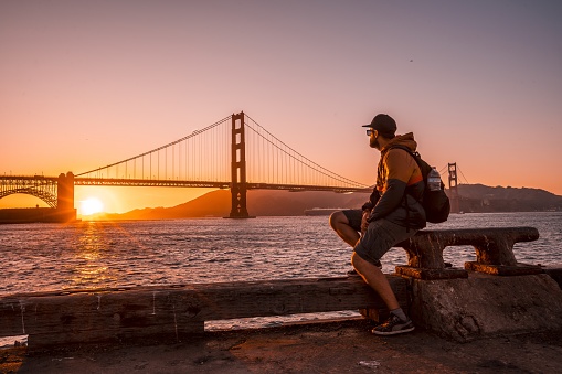 A man sitting in front of the Golden Gate Bridge during a sunset