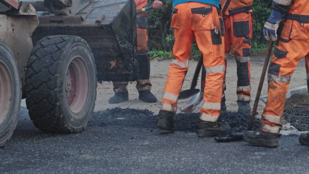 istock Roadwork Physical Workers in Protective Work Wear Repairing Street Tarmac Surface with Hot Asphalt 1439432012